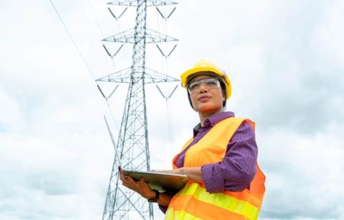 Utility worker with tablet in front of transmission line